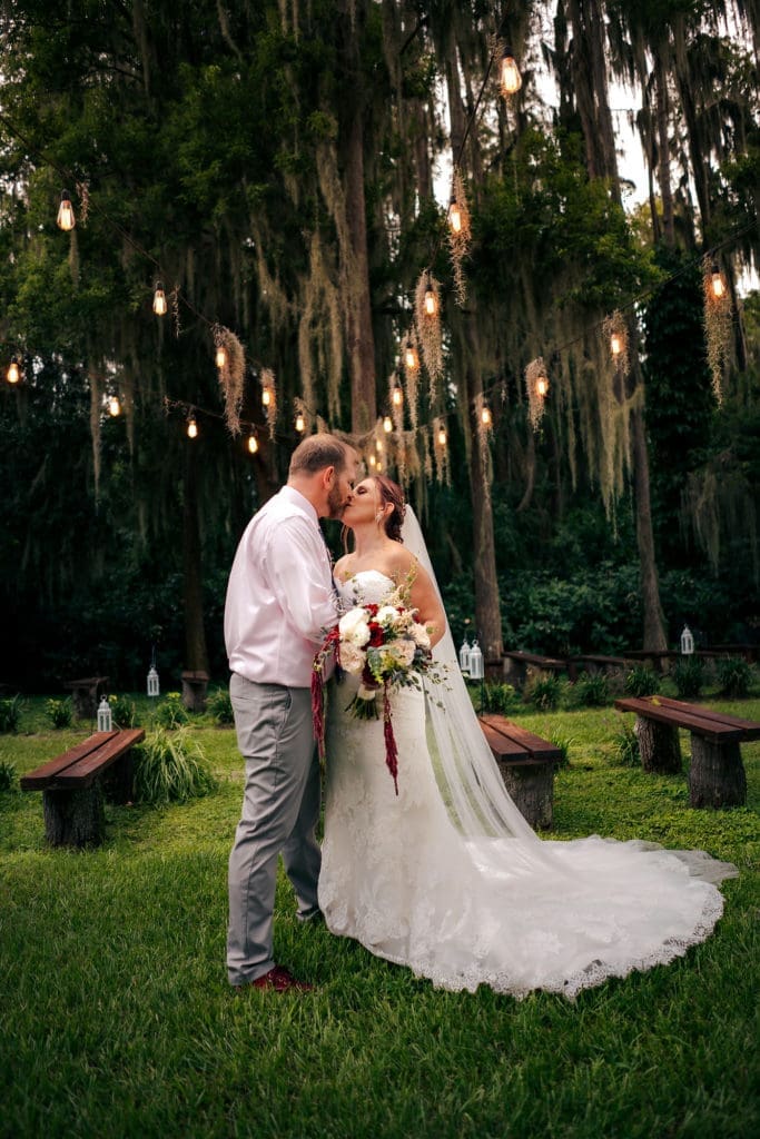 Bride and groom kissing in front of aisle under market lights at Knotted Roots on the Lake - Land O' Lakes