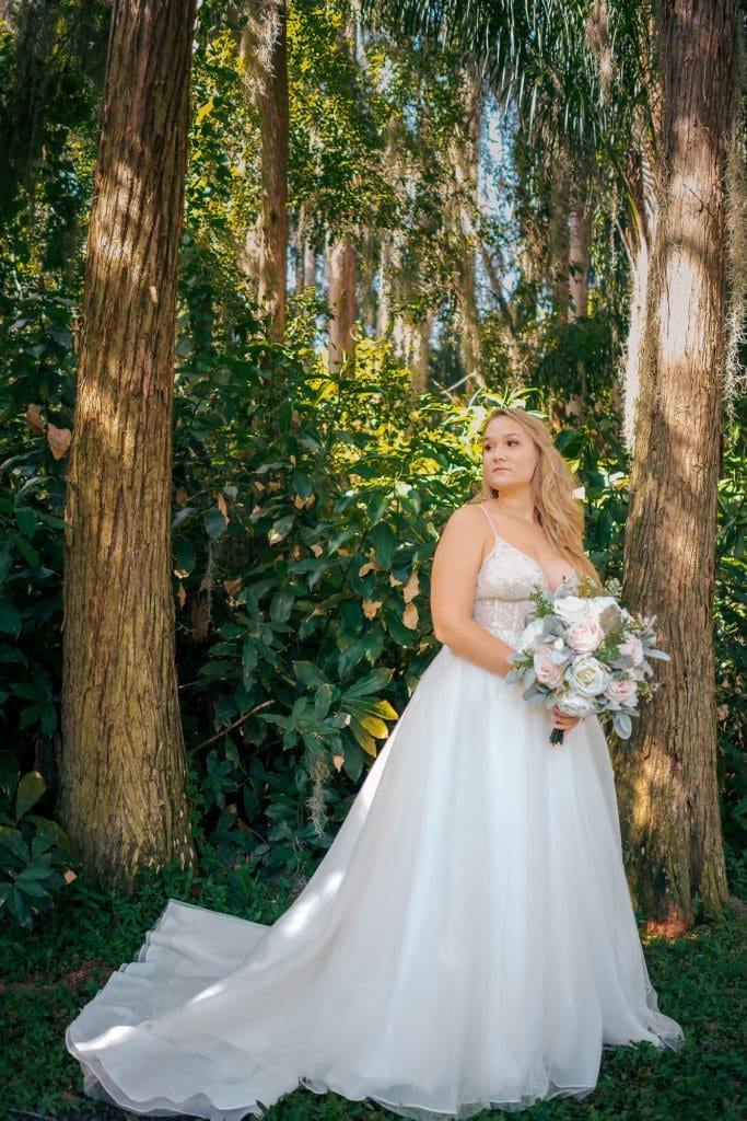 Bride holding bouquet under trees at Knotted Roots on the Lake